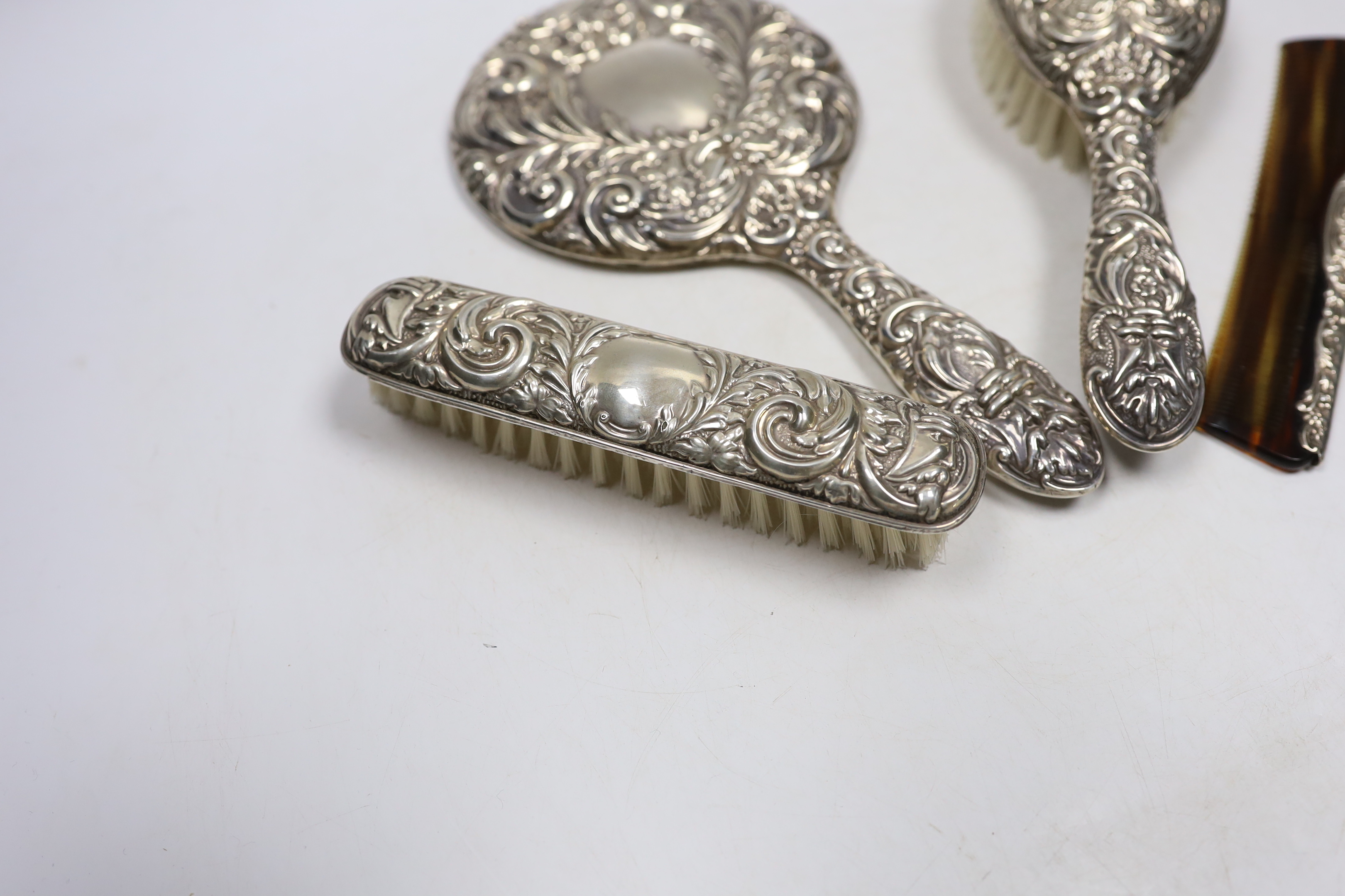 A modern repousse silver mounted hand mirror, two brushes and a comb.